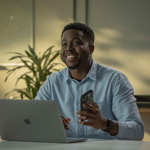 Abdul-Latif Amadu, Devops Engineer at Signable sat at laptop smiling in distance with phone half raised.